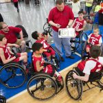 Jovens jogadores de basquete em cadeiras de rodas conversam com o treinador durante uma partida.