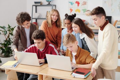 Estudantes colaboram em laptops em uma sala de aula, orientados por um professor.