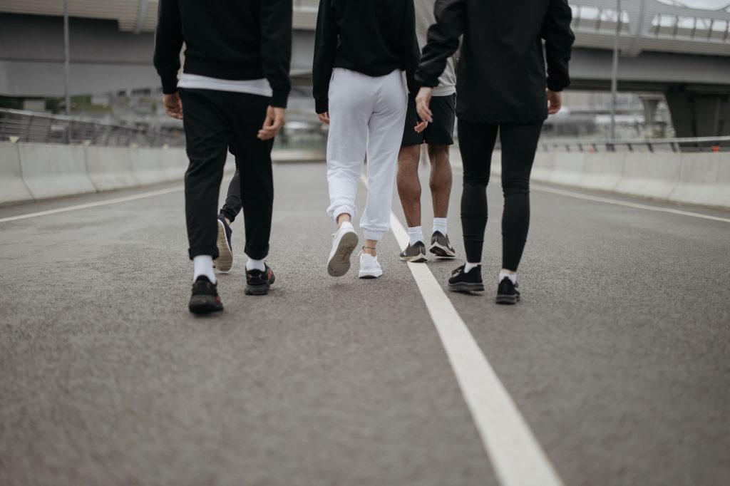 Caminhada reúne 350 pessoas em ação de saúde mental em Guarulhos Grupo de pessoas caminha por uma via urbana, visto de costas, usando roupas esportivas.