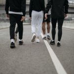 Grupo de pessoas caminha por uma via urbana, visto de costas, usando roupas esportivas.