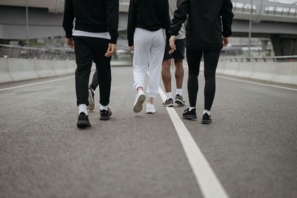 Grupo de pessoas caminha por uma via urbana, visto de costas, usando roupas esportivas.