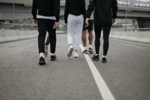 Grupo de pessoas caminha por uma via urbana, visto de costas, usando roupas esportivas.