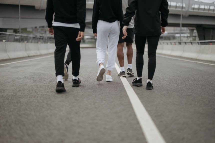 Grupo de pessoas caminha por uma via urbana, visto de costas, usando roupas esportivas.