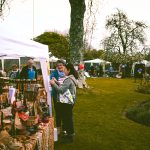 Feira ao ar livre em um parque, com visitantes circulando entre barracas de produtos artesanais.
