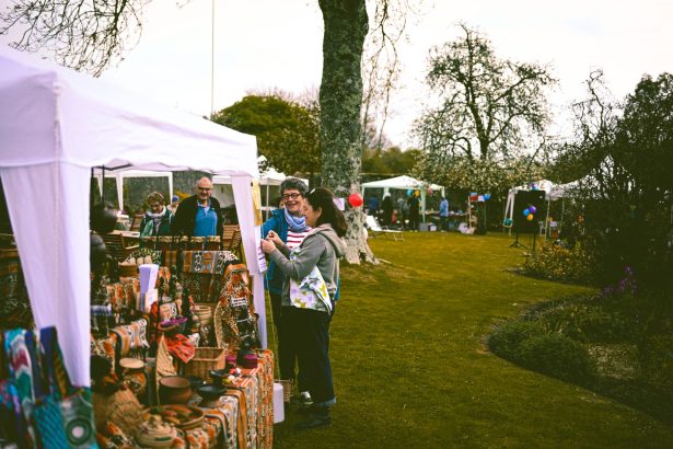 Feira ao ar livre em um parque, com visitantes circulando entre barracas de produtos artesanais.