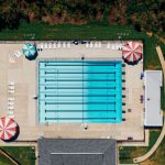Vista aérea de uma piscina pública ao ar livre cercada por áreas de apoio e vegetação.