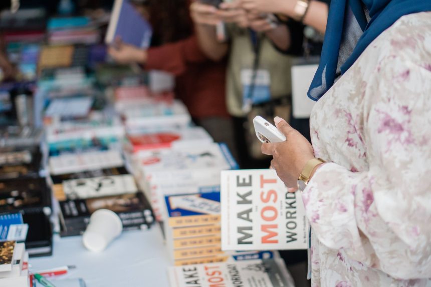 Livros expostos em uma feira literária enquanto visitantes circulam e observam os títulos.