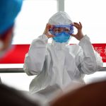Profissional de saúde veste equipamento de proteção dentro de um aeroporto.