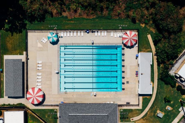 Vista aérea de uma piscina pública ao ar livre cercada por áreas de apoio e vegetação.