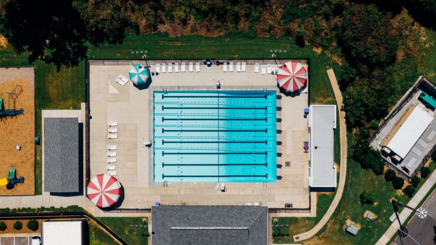 Vista aérea de uma piscina pública ao ar livre cercada por áreas de apoio e vegetação.