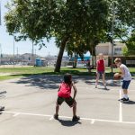 Grupo de crianças joga basquete em uma quadra esportiva ao ar livre.