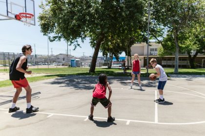 Grupo de crianças joga basquete em uma quadra esportiva ao ar livre.