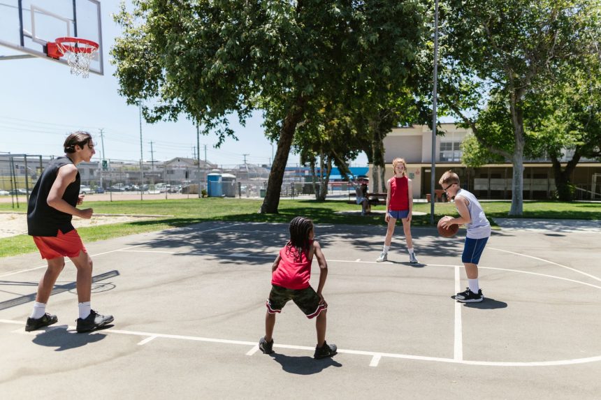 Grupo de crianças joga basquete em uma quadra esportiva ao ar livre.