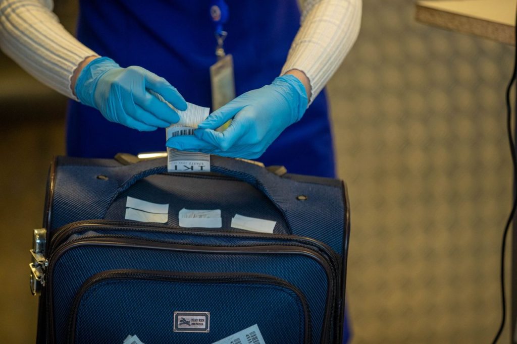 Mãos enluvadas de um agente inspecionam etiquetas de bagagem durante um procedimento de segurança no aeroporto.