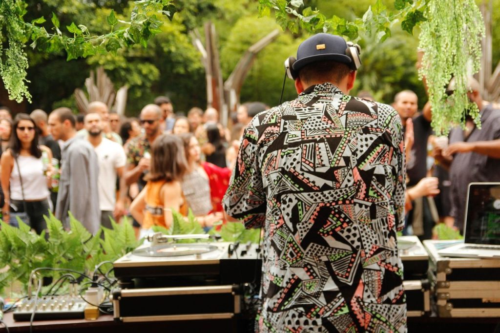 DJ se apresenta ao ar livre diante de um público, em meio à vegetação.
