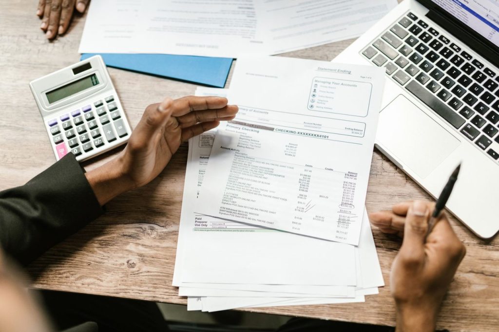 Empresas de Guarulhos terão de revisar integração fiscal antes de mudança na NFS-e Mãos seguram documentos financeiros ao lado de uma calculadora e um laptop em uma mesa de escritório.