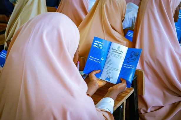 Mulheres participam de uma atividade educativa sobre saúde mental e consultam um folheto em uma sala.