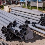 Tubulações de PVC cinza empilhadas em um canteiro de obras ao ar livre.