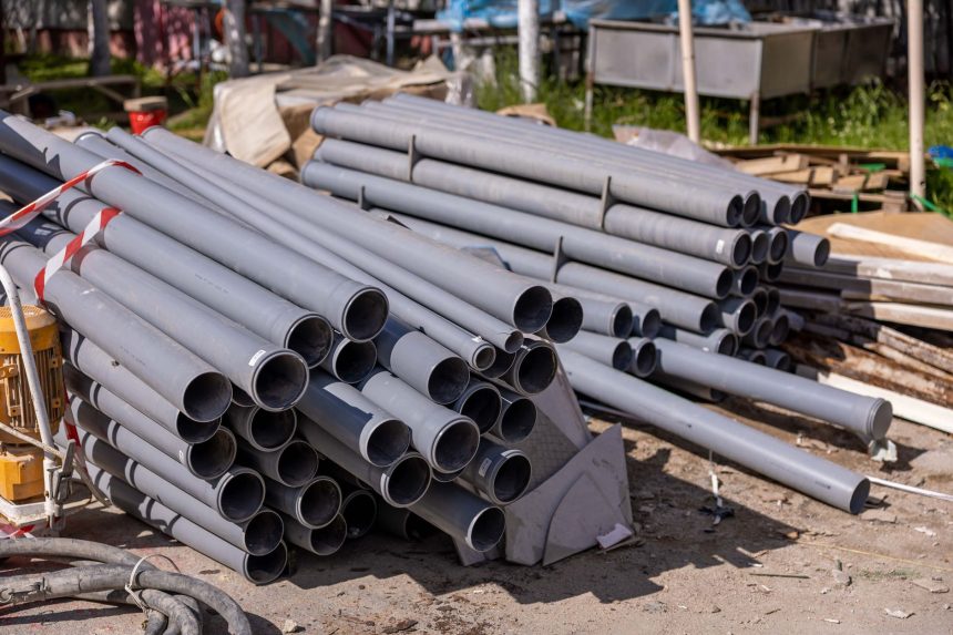 Tubulações de PVC cinza empilhadas em um canteiro de obras ao ar livre.