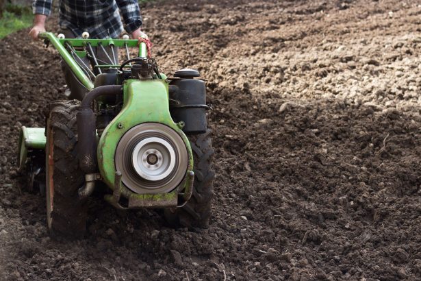 Agricultor opera um trator de pequeno porte em campo recém-arado para preparar o solo.